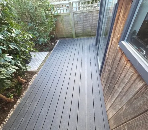 Composite decking laid up to the doors of a timber clad garden room, with a gravel margin along the edge.