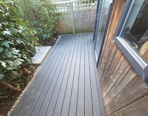 Composite decking laid up to the doors of a timber clad garden room, with a gravel margin along the edge.