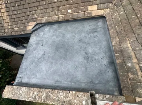 A lead flat roof laid between stone slate slopes, dressed up to the tiles around it.