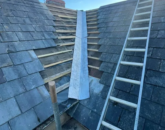 A slate roof valley stripped back to new battens, with new lead run down it.