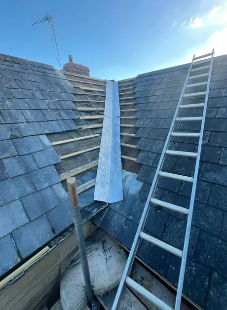 A slate roof valley stripped back to new battens, with new lead run down it.