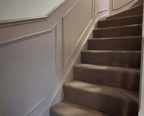 Moulded panelling run up a staircase wall, following the rake of the stairs, with a cap rail along the top.