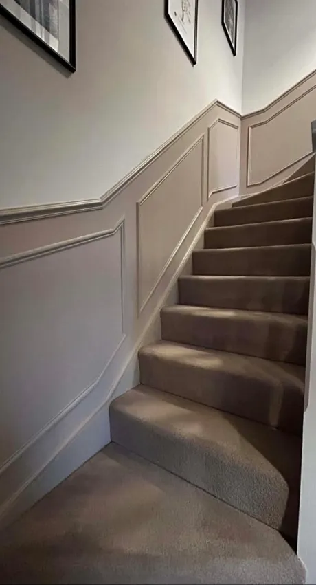 Moulded panelling run up a staircase wall, following the rake of the stairs, with a cap rail along the top.