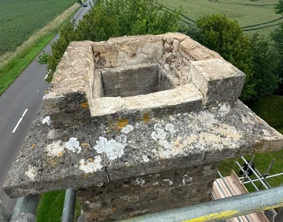 A stone chimney stack with the cap cracked through and the mortar gone from the joints.