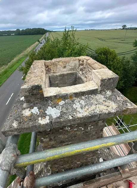 A stone chimney stack with the cap cracked through and the mortar gone from the joints.
