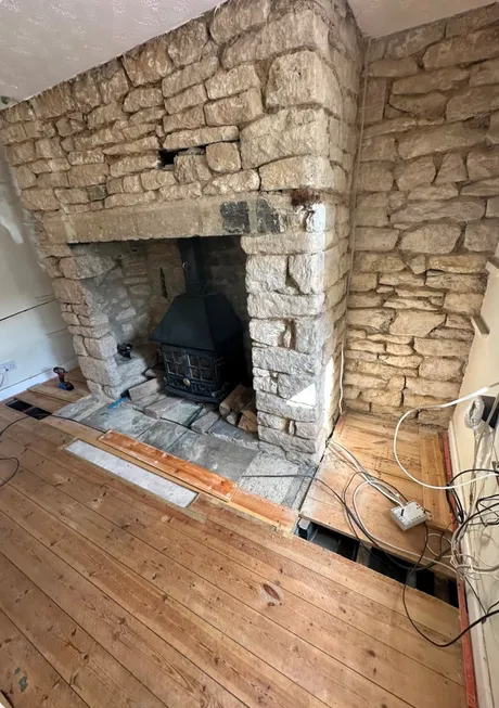 A stone inglenook with a cast iron stove in the opening, the chimney breast back to bare stone and the floor up in front of it.