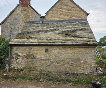 A Cotswold stone slate roof laid in diminishing courses on a stone outbuilding, with lead run along the top edge where it meets the gable wall.