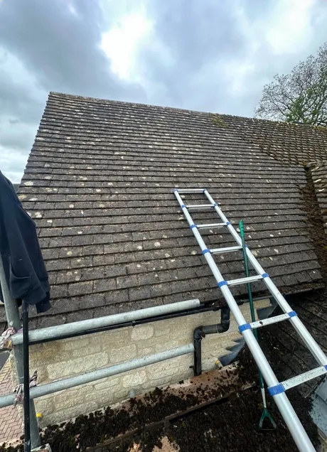 An old Cotswold stone slate roof with moss through the lower courses, scaffolded at the eaves.
